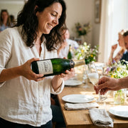 NV Mousse  - Champagne Extra-Brut Blanc de Noirs Eugene | Create an ultra-photorealistic image centered on the uploaded NV Mousse - Champagne Extra-Brut Blanc de Noirs Eugene, depicted being served at a lively celebrat