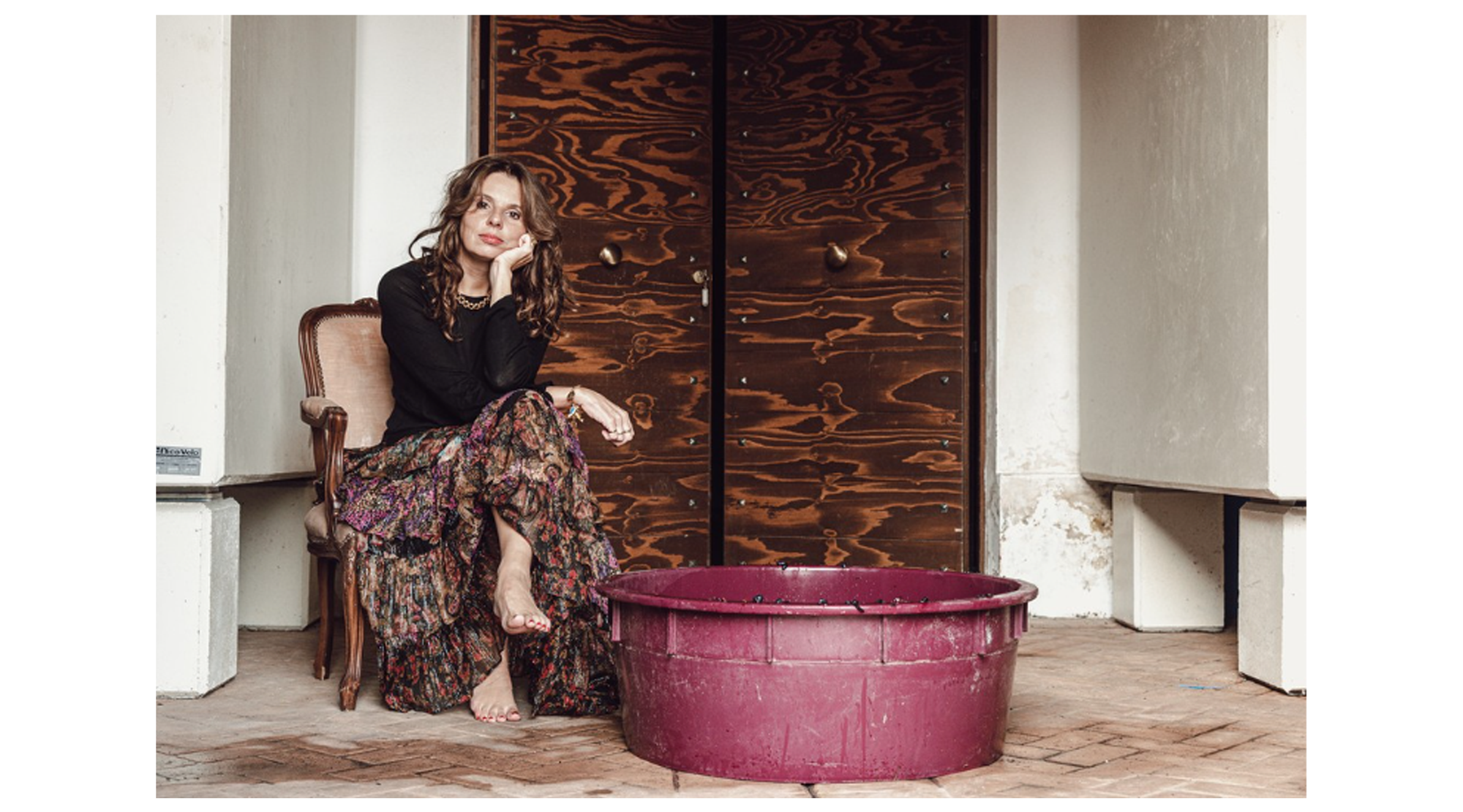 Woman sitting on a chair next to a large purple basin in a room with wooden doors.